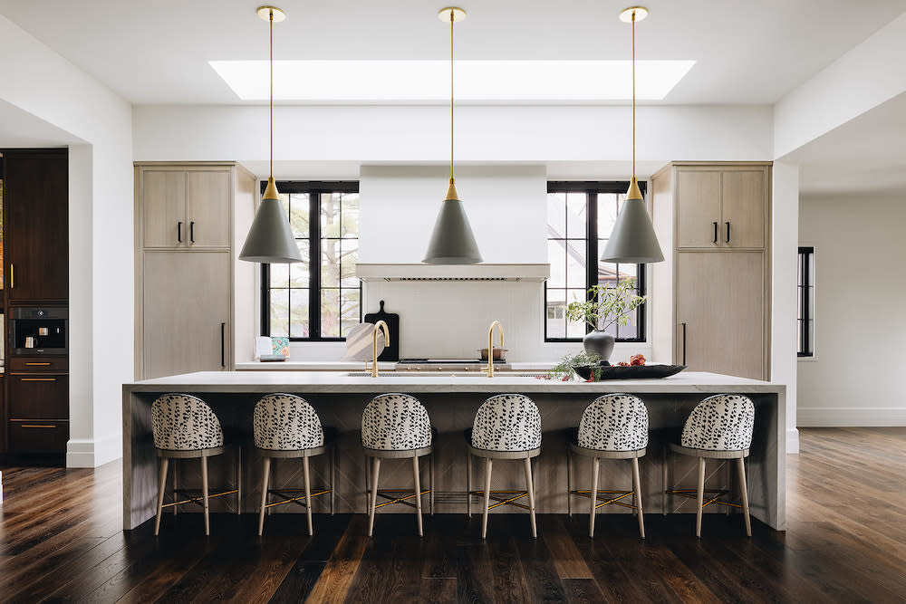 This light contemporary kitchen with light wood cabinets, center island, black and white counter stools, dual sinks and pendant lighting.