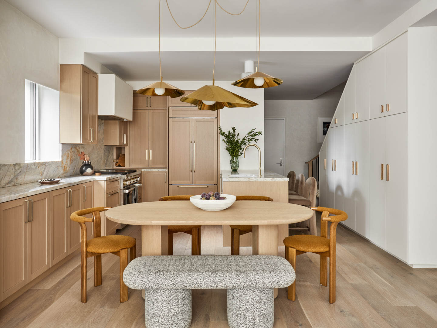 Modern kitchen with light wood cabinetry, marble countertops, and gold pendant lighting. A cozy dining area features a wooden table and stylish chairs.
