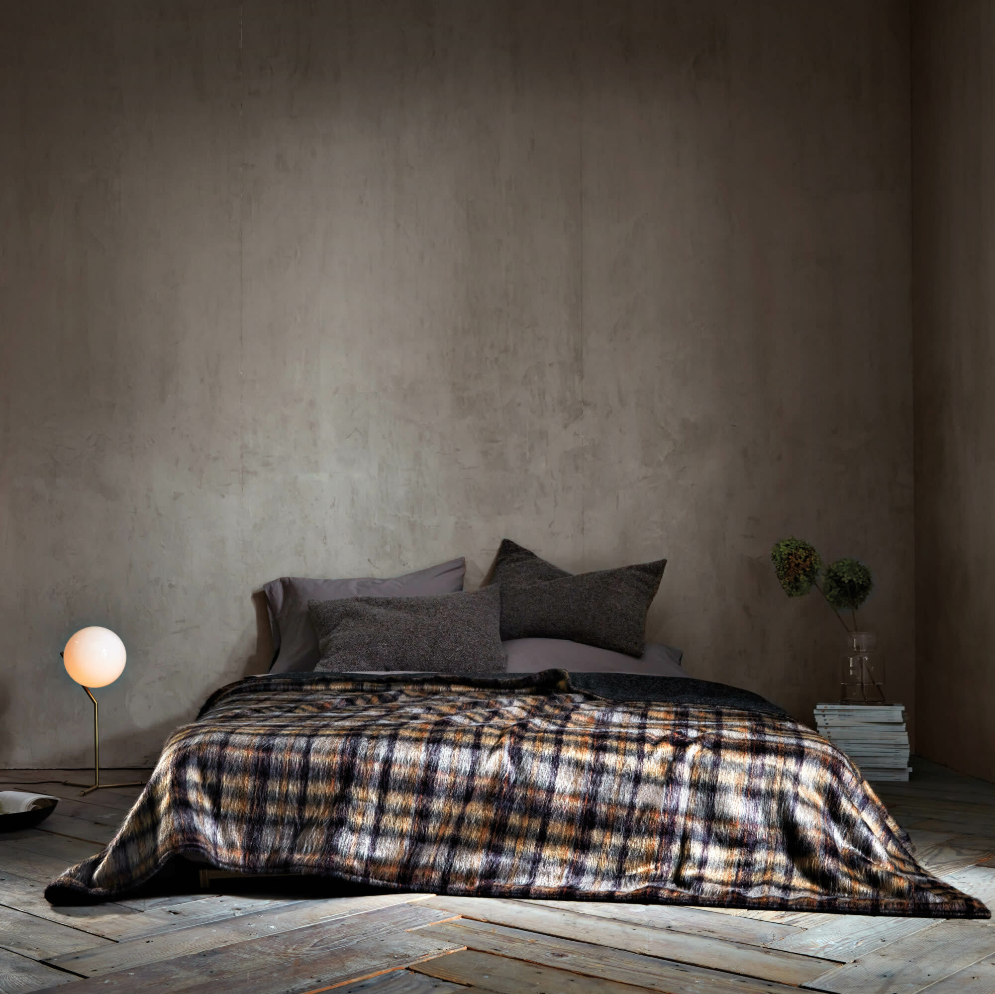 Bedroom with herringbone wood floors and bed with dark-colored pillows and plaid blanket against gray wall.