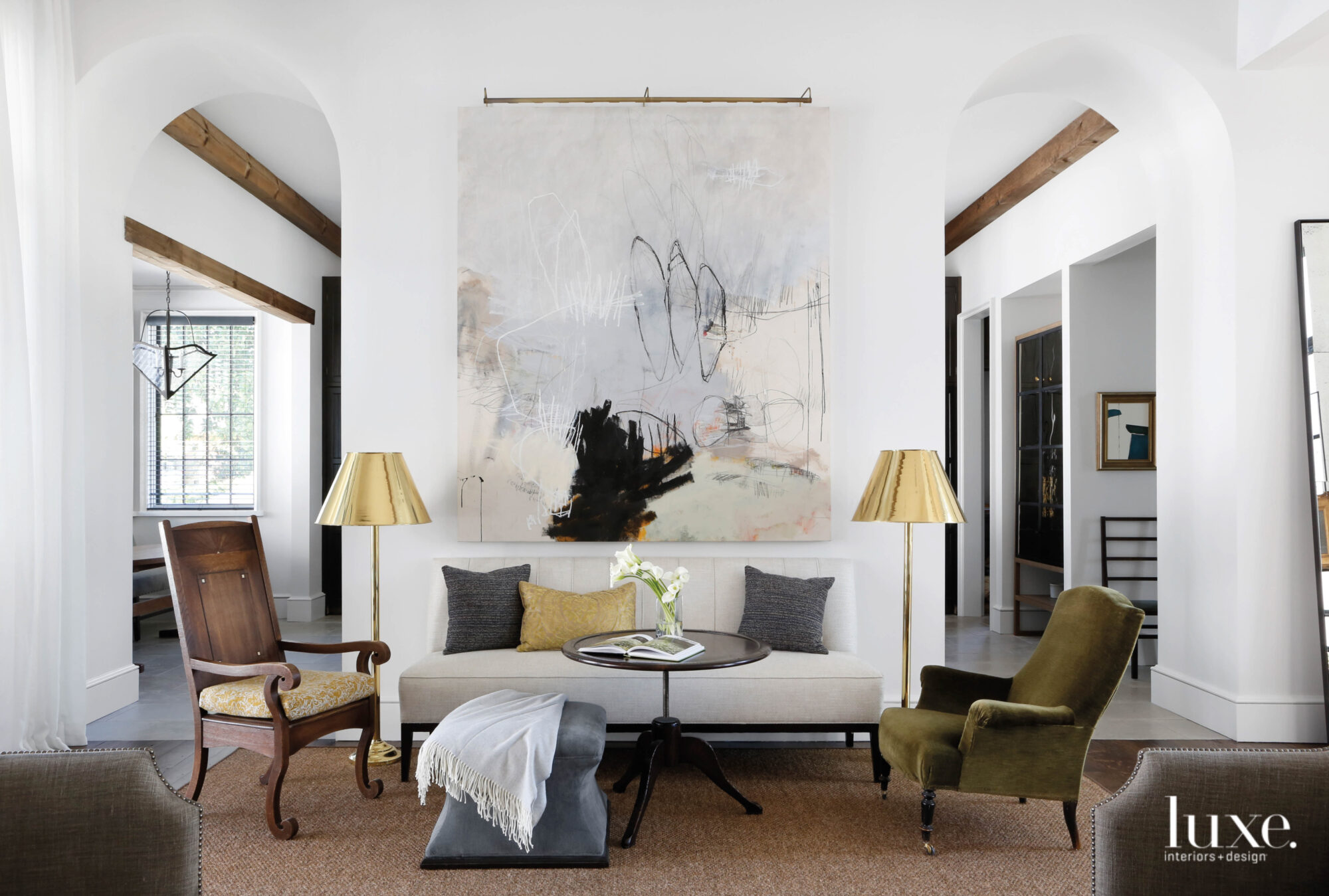 A seating group with a settee, mismatched armchairs, cocktail table, pair of polished brass floor lamps and large-scale abstract painting