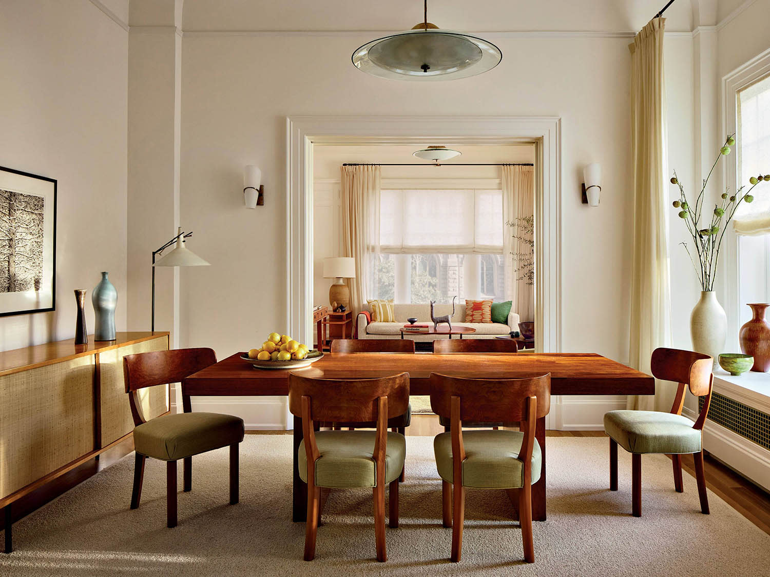 A dining table, chairs and credenza, with a chandelier above and open doorway into a sitting room.
