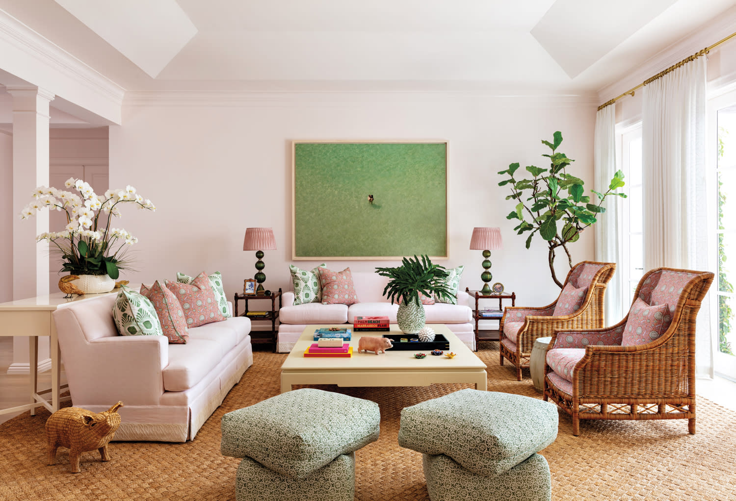 living area with light pink walls, green artwork, pink sofas and rattan armchairs in home by Sara McCann