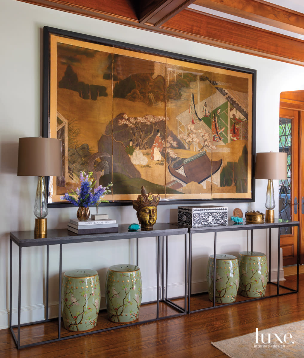 A Chinese screen hangs above a long console table and a series of ceramic stools.