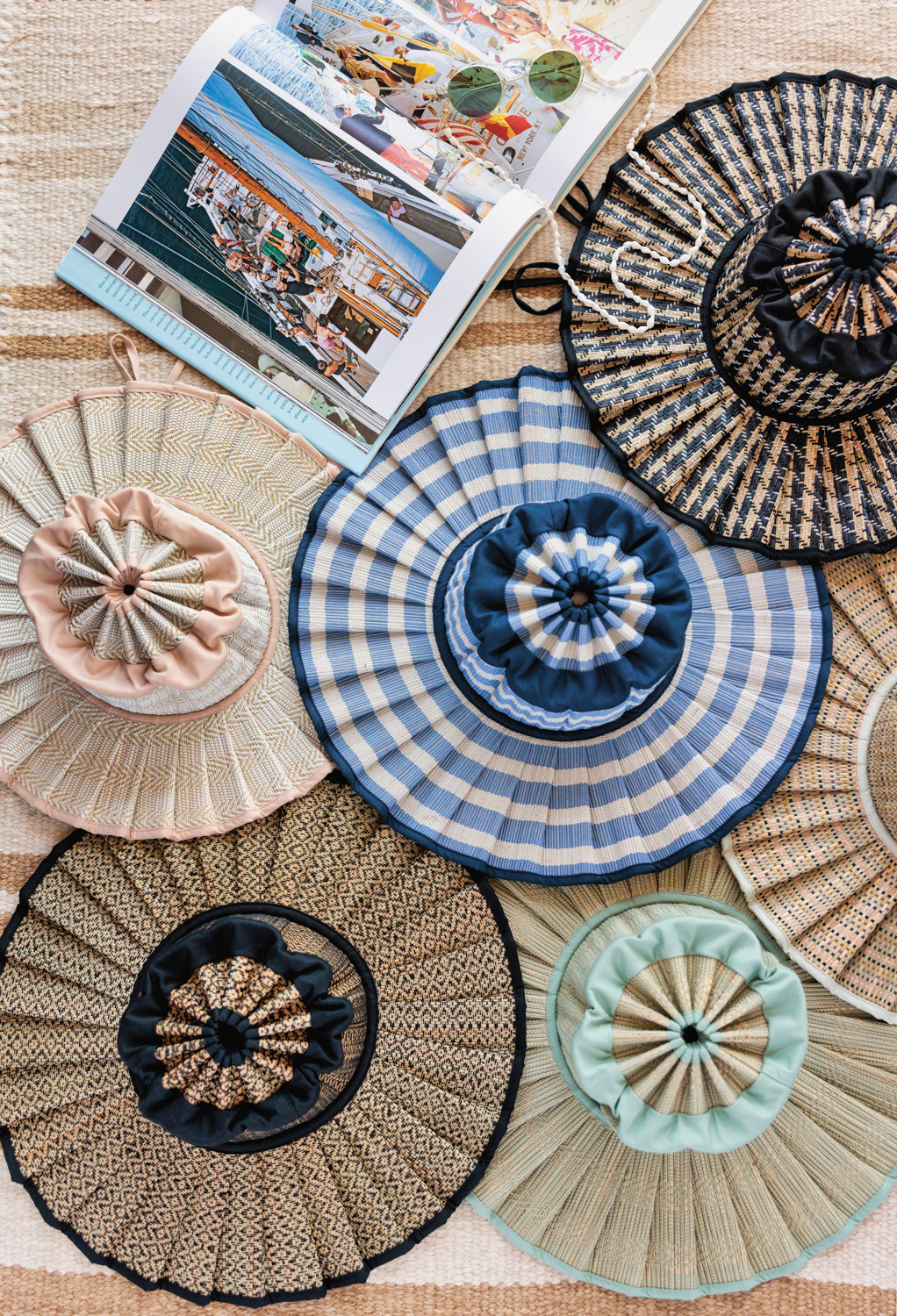 Overhead shot of 6 Lorna Murray hats beside an open photography book and sunglasses