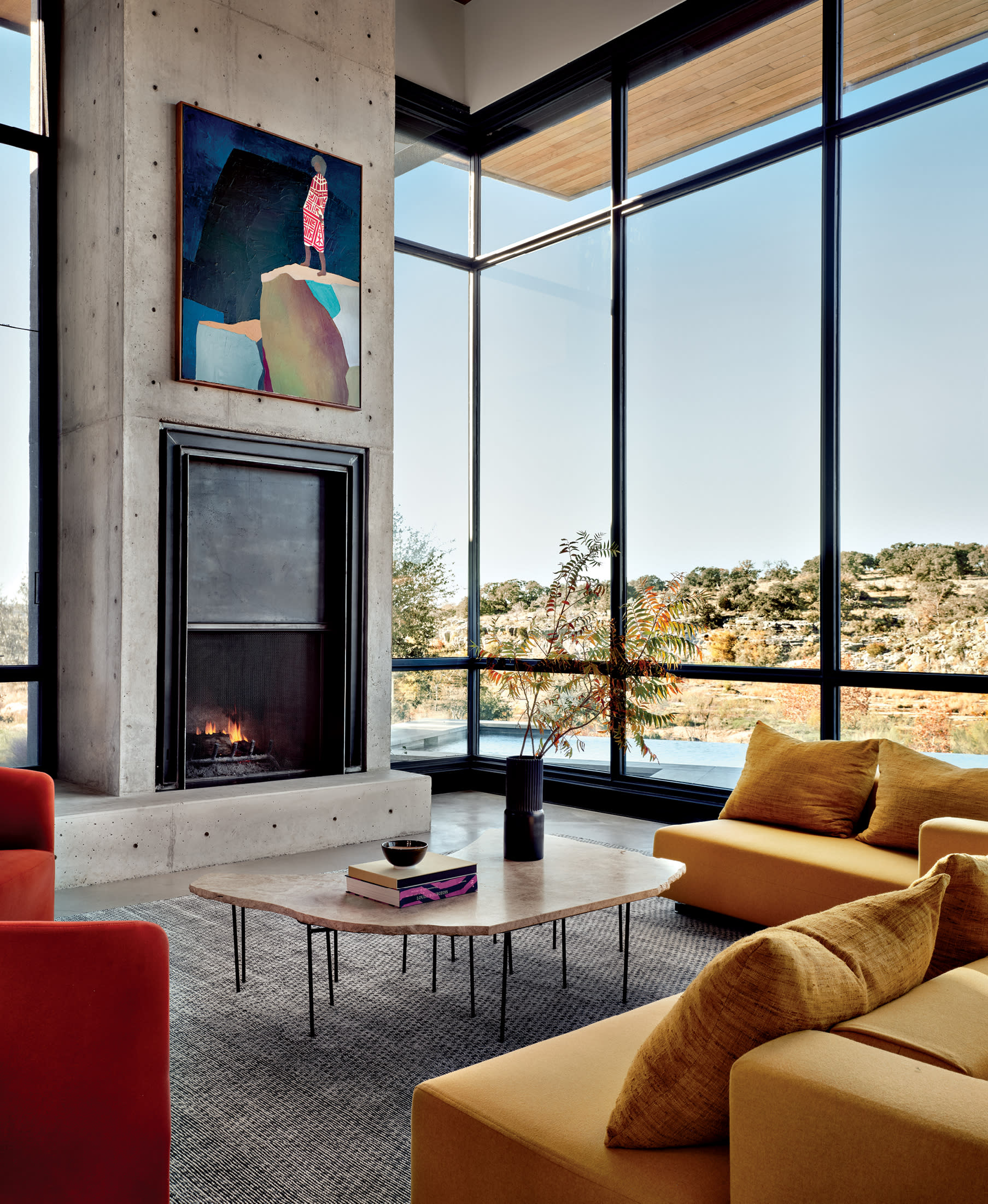 industrial living room with a concrete-framed fireplace, floor-to-ceiling windows and pops of color