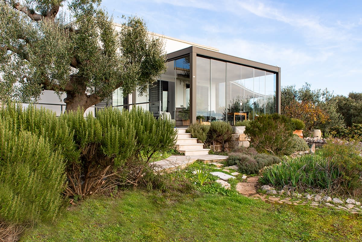 A house with a large tree in the front yard and a see-through structure in the backyard.