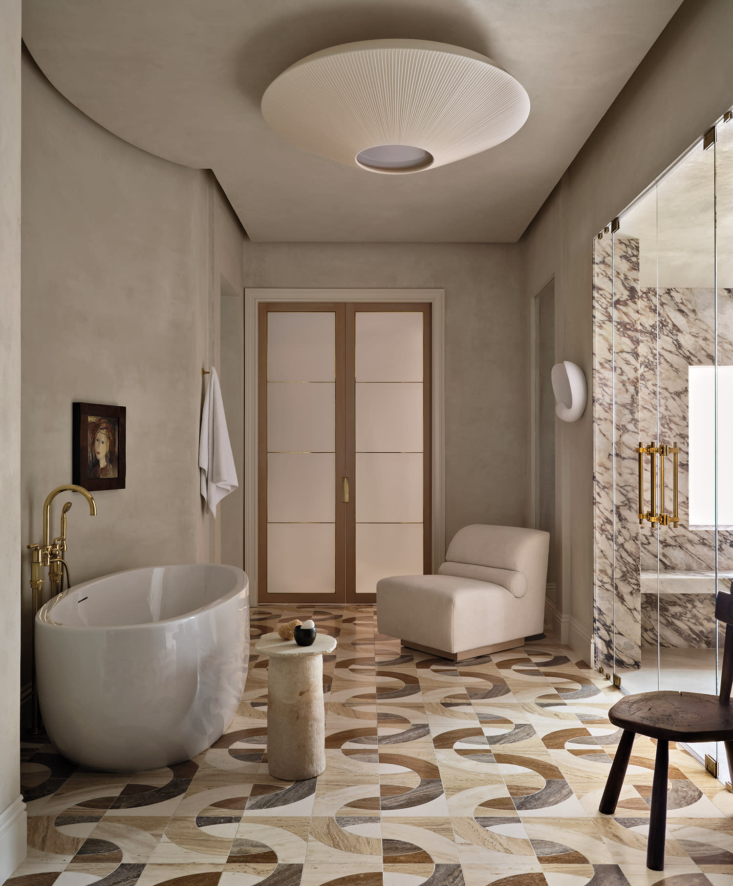 Elegant bathroom with a modern oval bathtub, geometric tile floor, marble shower, soft armchair, and warm lighting.