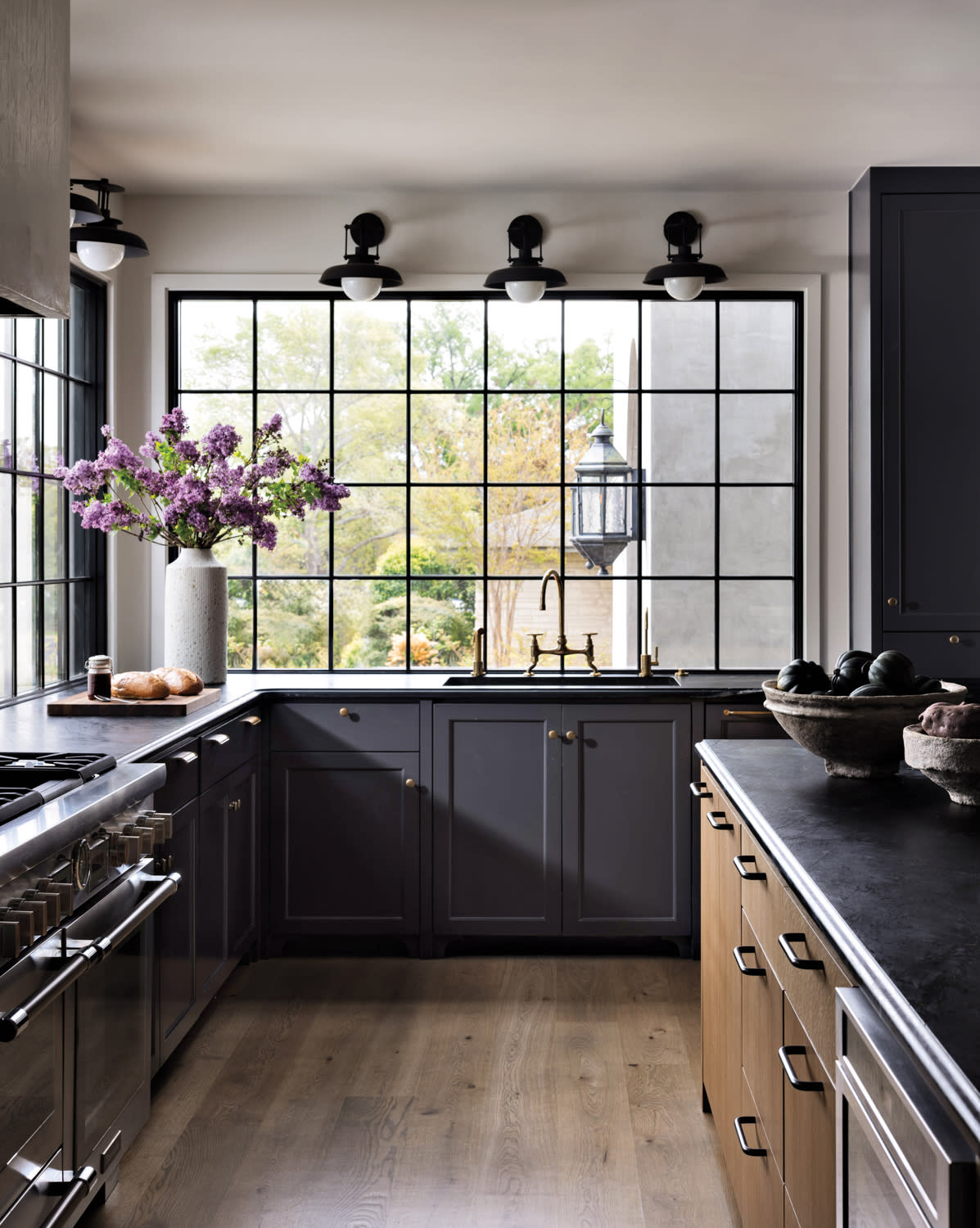 A kitchen with a refrigerator and stove, wood cabinetry, an island and bright windows with sconces.