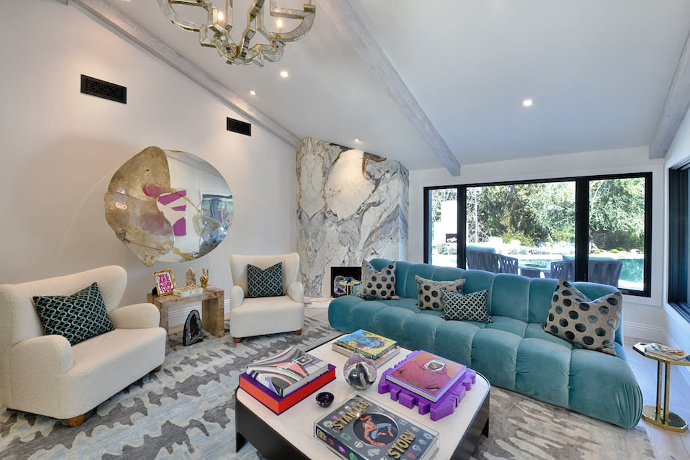 A living room featuring blue couches, coffee table books, and a wall-mounted mirror.