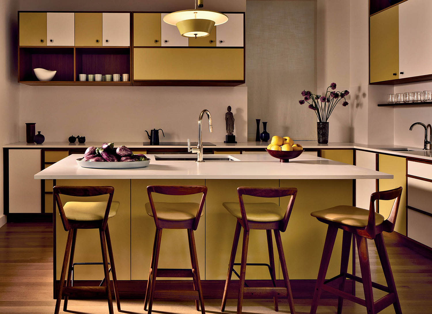A kitchen painted in white and yellow, with overhead cabinets and a central island with stools.