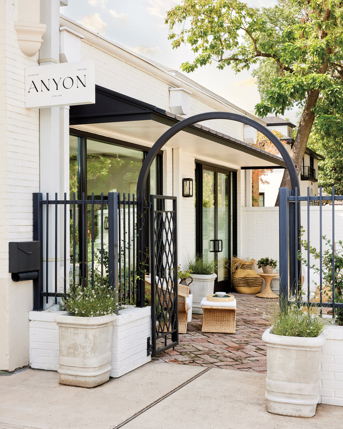 White brick shop façade with iron arch and fencing leading the way to a brick courtyard.