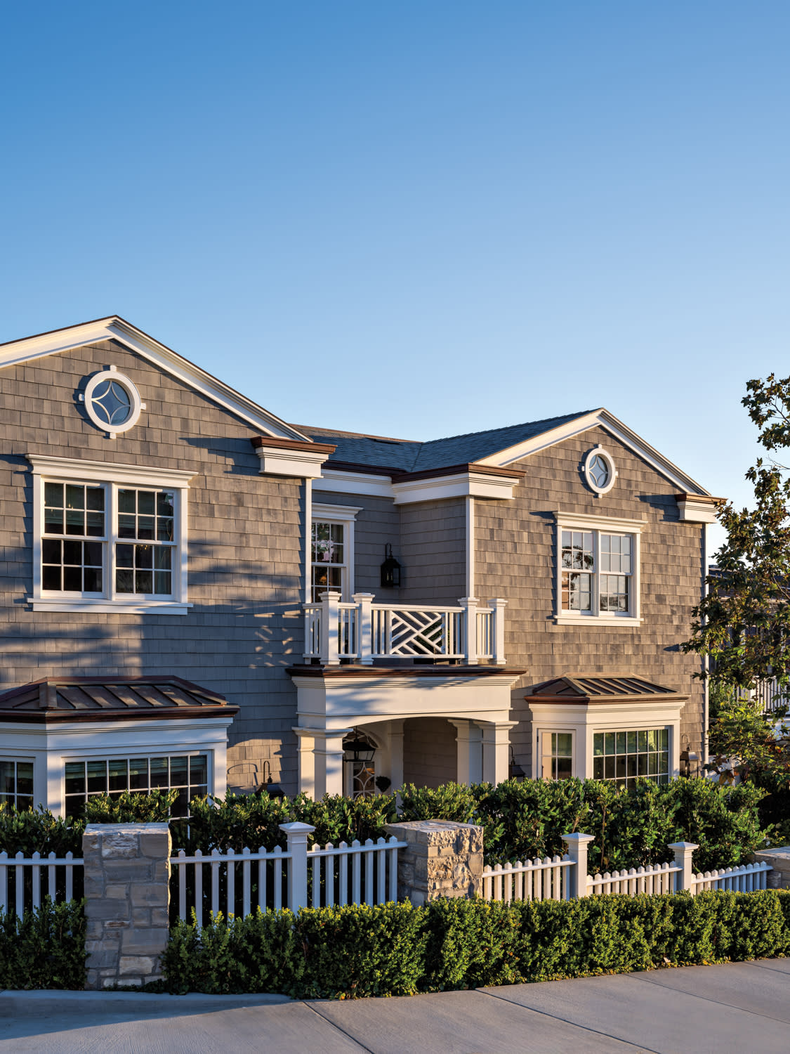 Facade of home by Anthony Laney with bay windows and a centered entrance, covered in cedar shingles in a gray stain