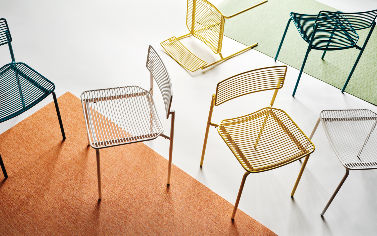 yellow, green and white wire chairs on top of a bright orange carpet