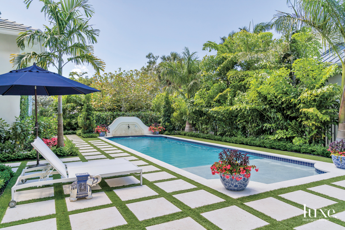 pool with blue and white pottery planters and a blue umbrella over a lounge chair