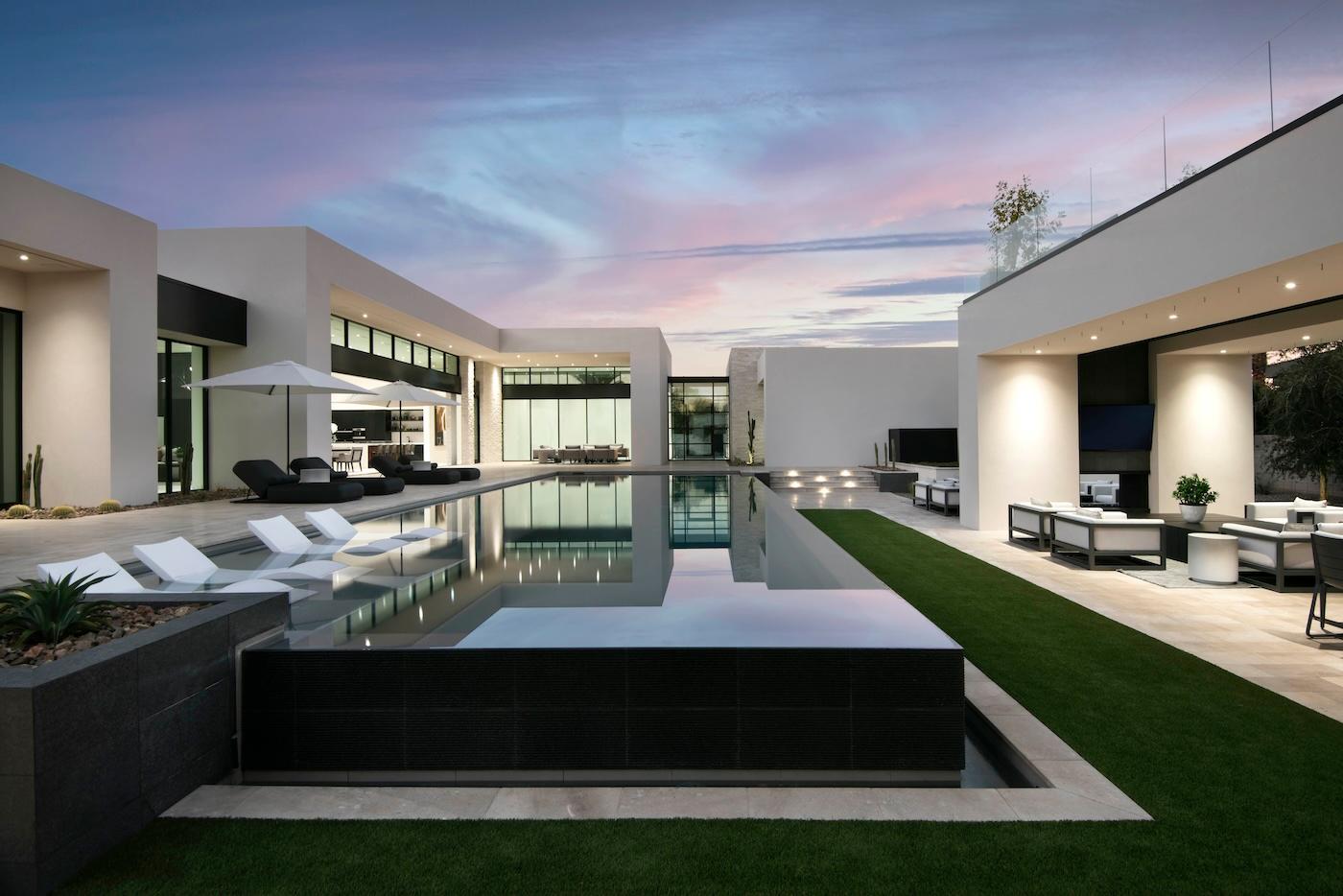 Modern luxury home with sleek architecture and large reflective pool. Minimalist patio furniture and evening sky convey a serene, elegant atmosphere.