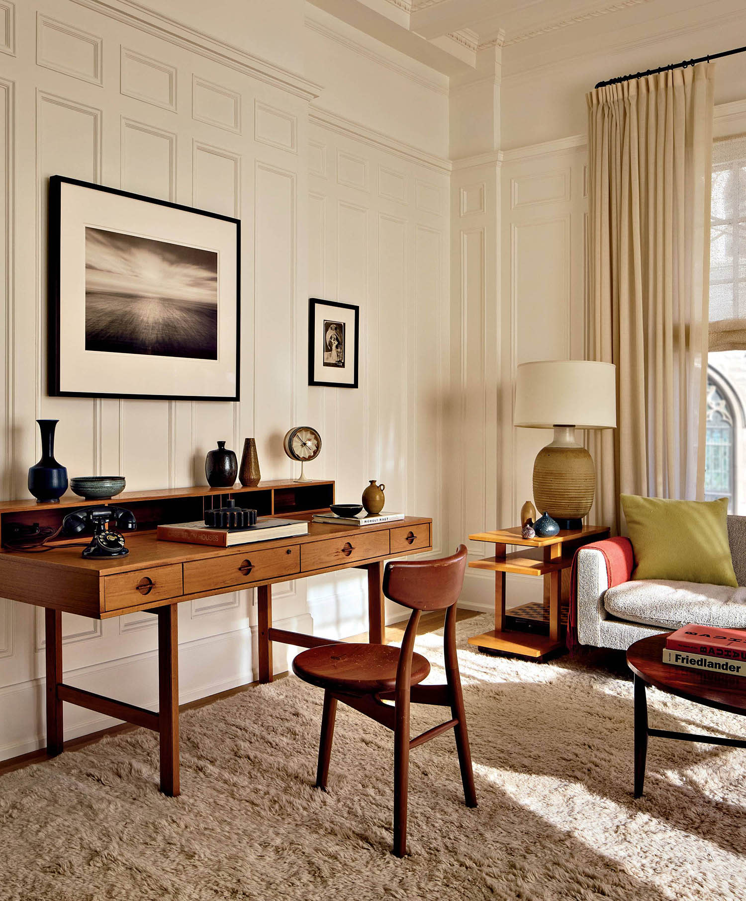 A desk and matching chair sit against a wall with white wood paneling and framed photography.