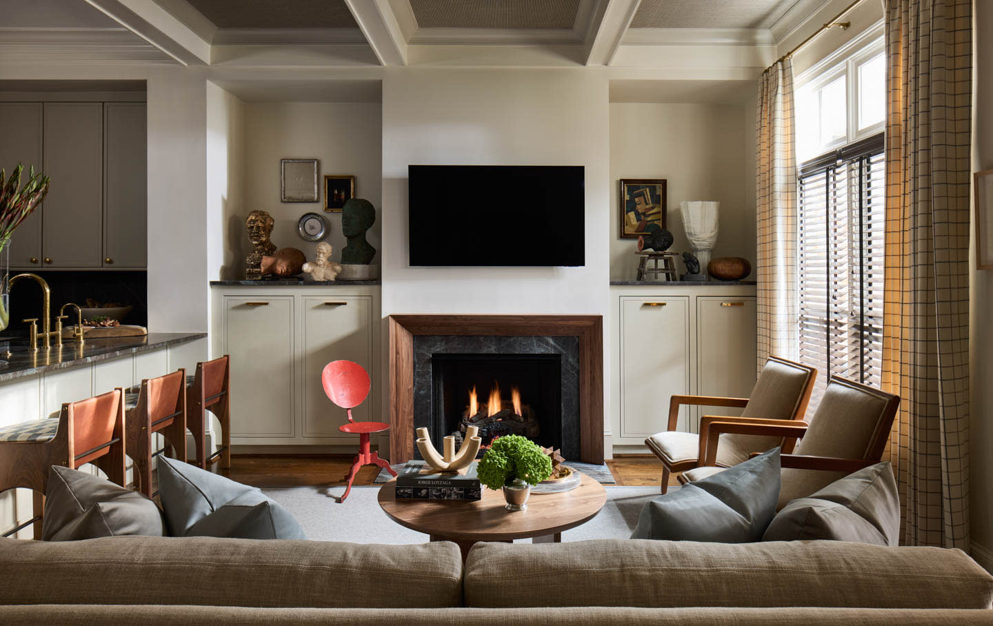 A cozy living room with a calming atmosphere, featuring a modern fireplace, wall-mounted TV, and a round wooden coffee table surrounded by neutral-colored sofas and chairs