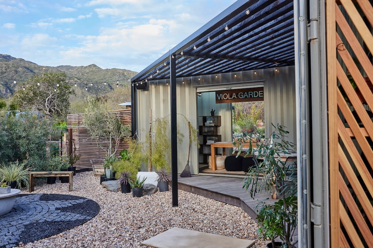 An outdoor patio with a central fire pit, adorned with lush plants, perfect for relaxation and gatherings.