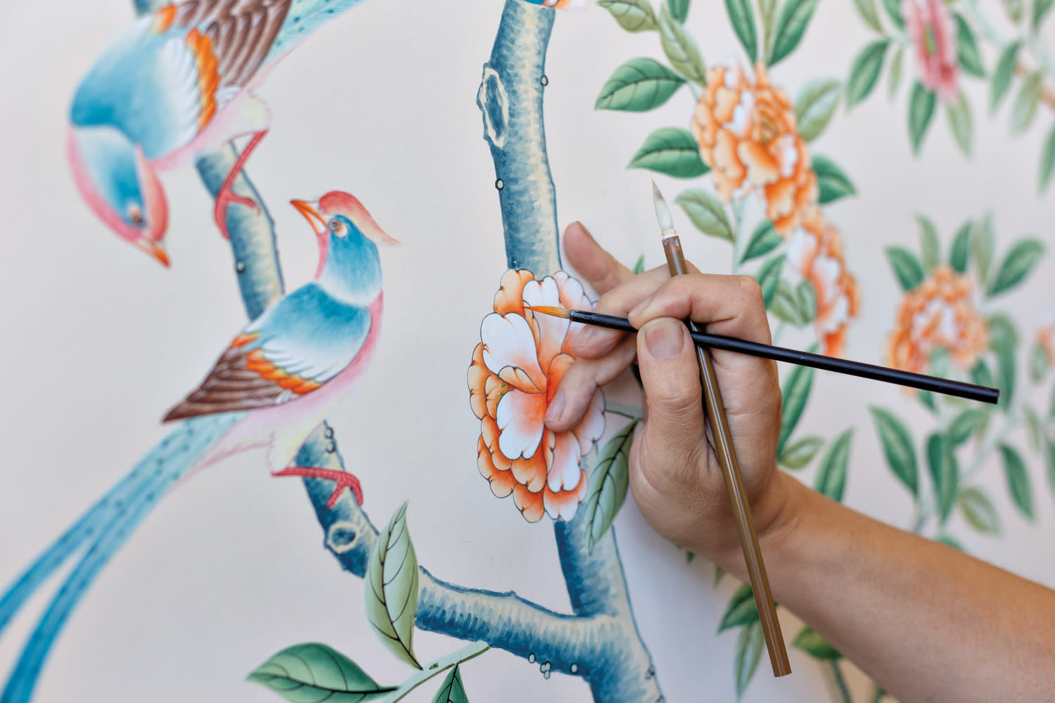 a person holds two brushes while painting a flower on wallpaper