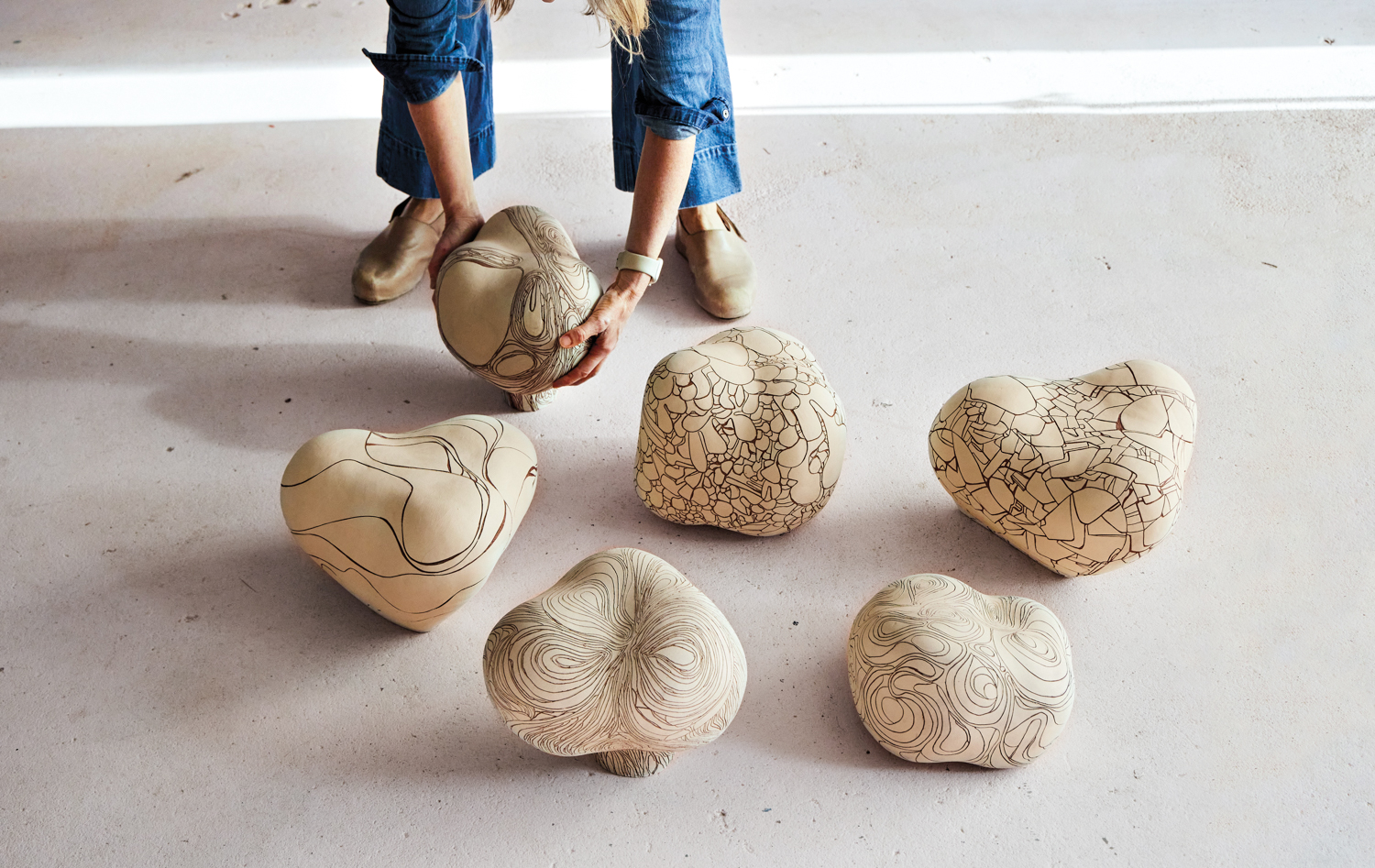 Woman standing before several rounded ceramic objects, picking one of them up off the floor