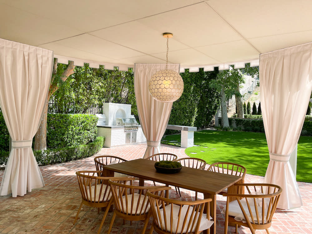 wood table and chairs under a curved patio with canopy and drapes