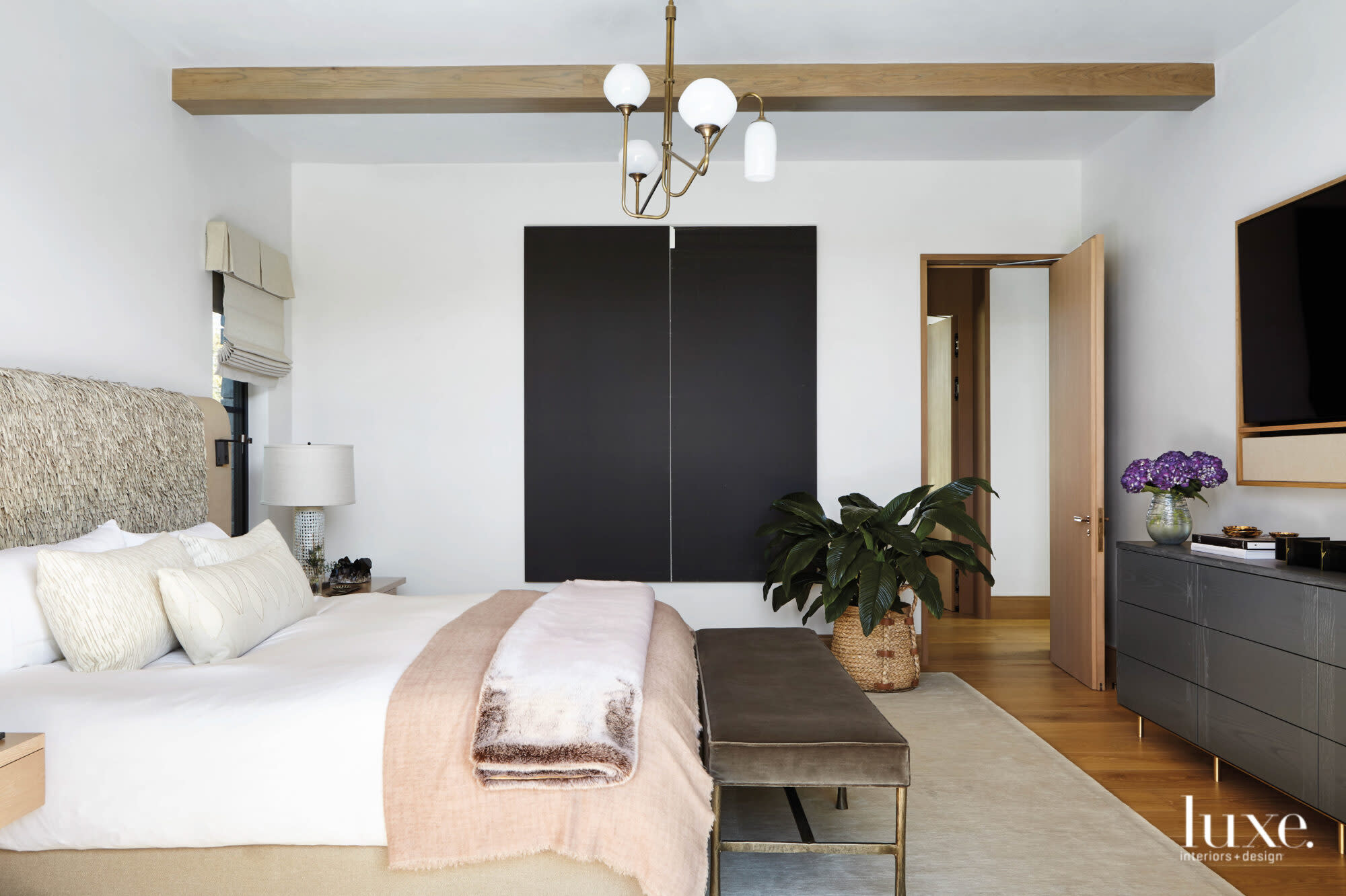 A bedroom has dark-hued art and a many-armed light fixture.