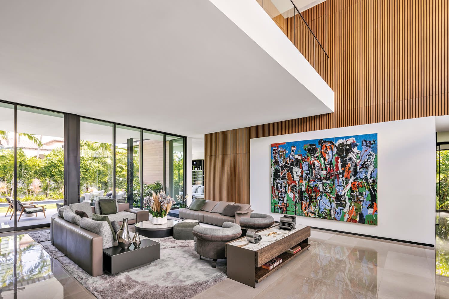 A contemporary home's living area with a wood wall, colorful artwork and taupe furnishings