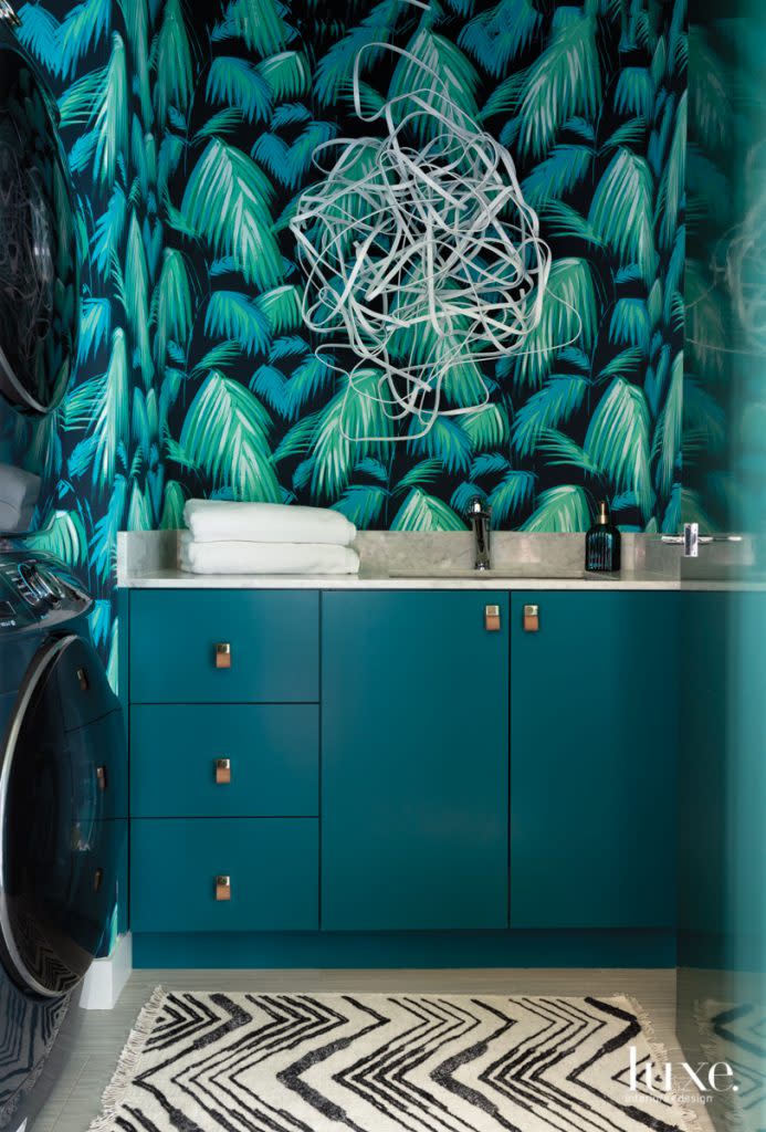 The utility room features a Matthew Williamson stylized palm-print wallpaper for Osborne & Little from ID Collection and sculpture by Matt Devine from Laura Rathe Fine Art. Shelton Builders. fabricated the cabinetry, which is painted Sherwin-Williams Really Teal.