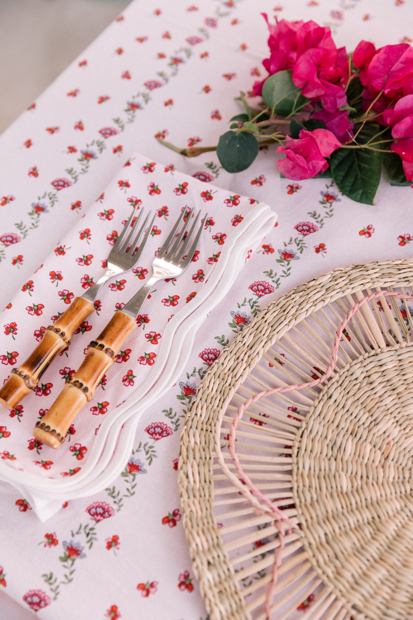 A rattan-detailed place-mat sits atop a colorful, floral tablecloth