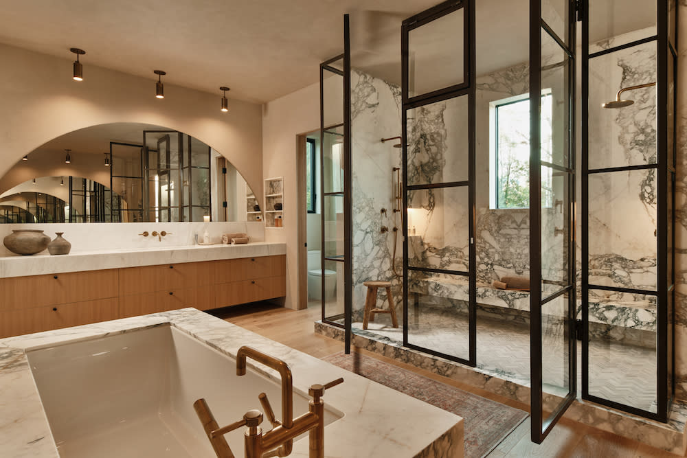 A modern bathroom featuring a spacious glass shower, marble walls and a stylish bathtub, creating a serene and elegant atmosphere.