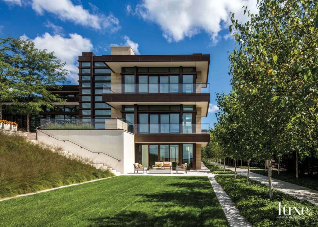 Nestled into a slope on the property, the home's lower level opens to a patio overlooking a large lawn bordered by a row of birch trees and a bed of natural grasses planted by Shane Coen.