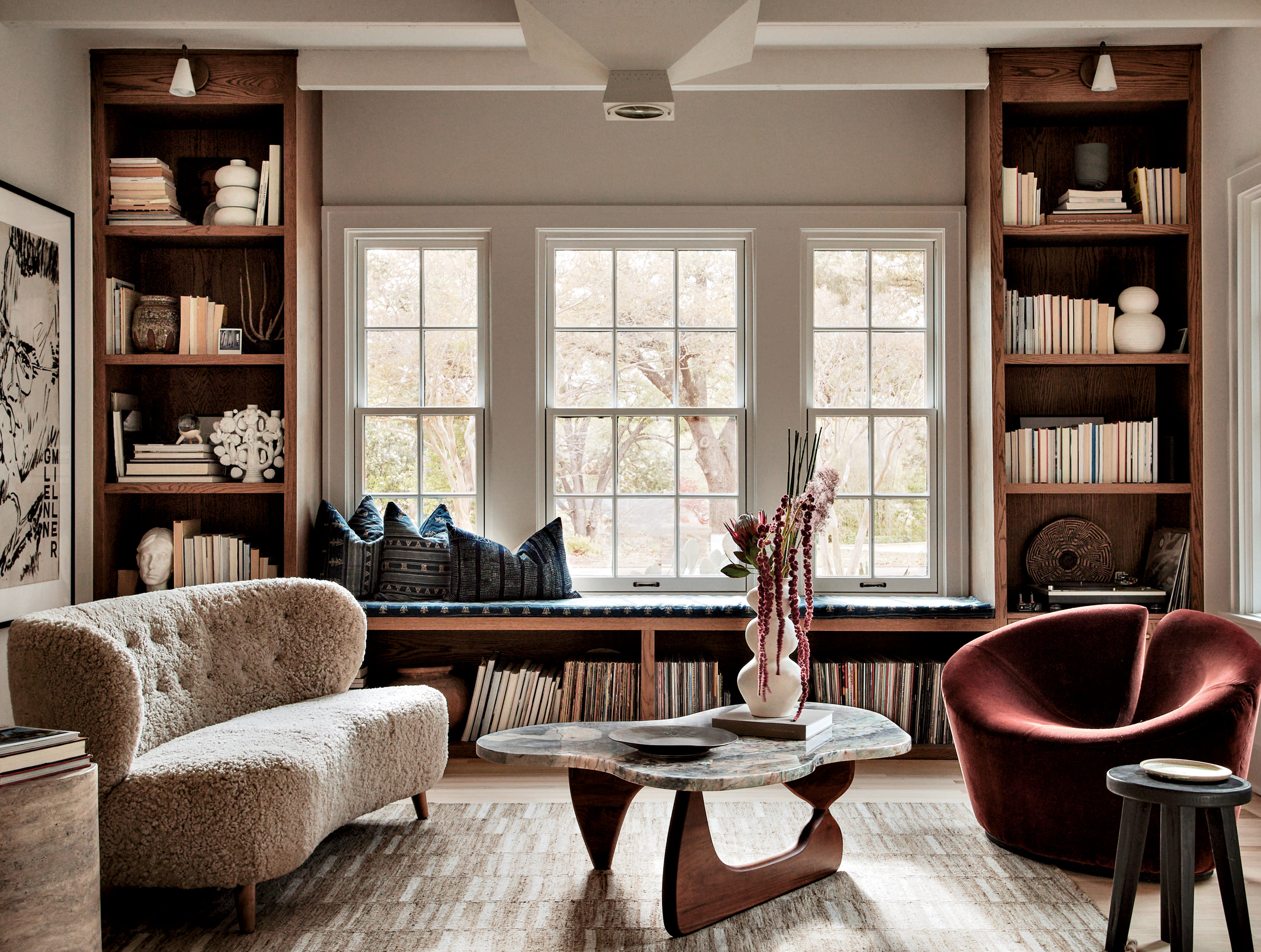 A sofa and angular chair sit on opposite sides of a coffee table near built-in shelves and window.