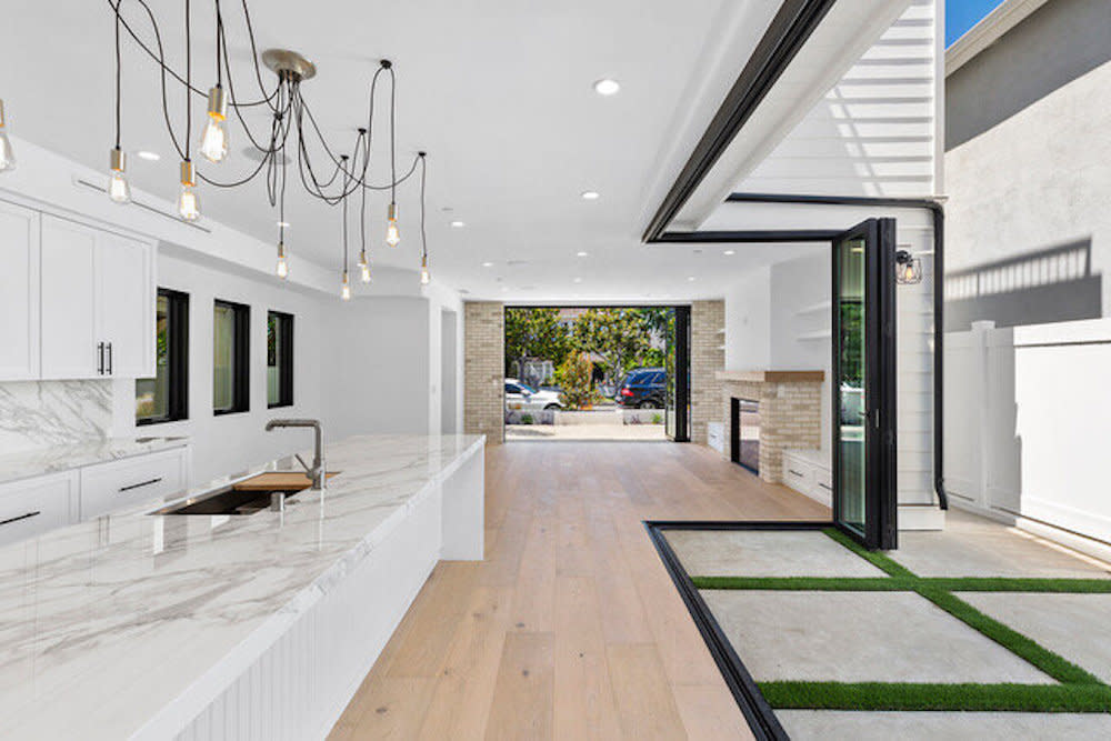 All white modern kitchen with marble countertops, pendant lighting and floor to ceiling doors that provide an indoor-outdoor living space.