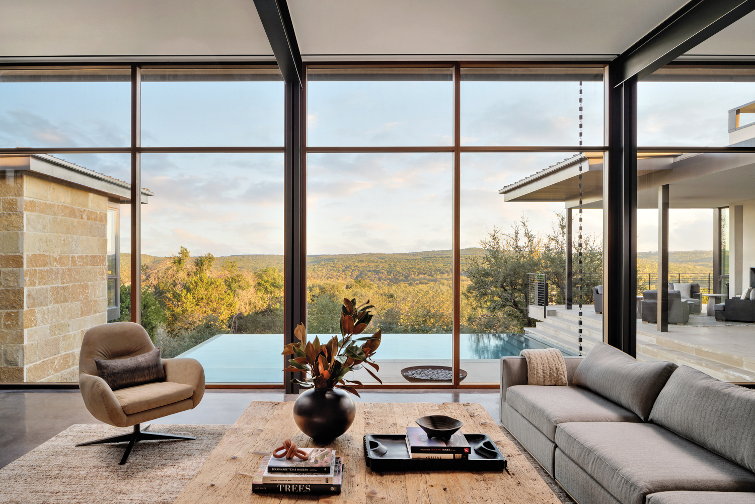 minimalist living room with floor to ceiling windows with views of an outdoor pool and rolling hills