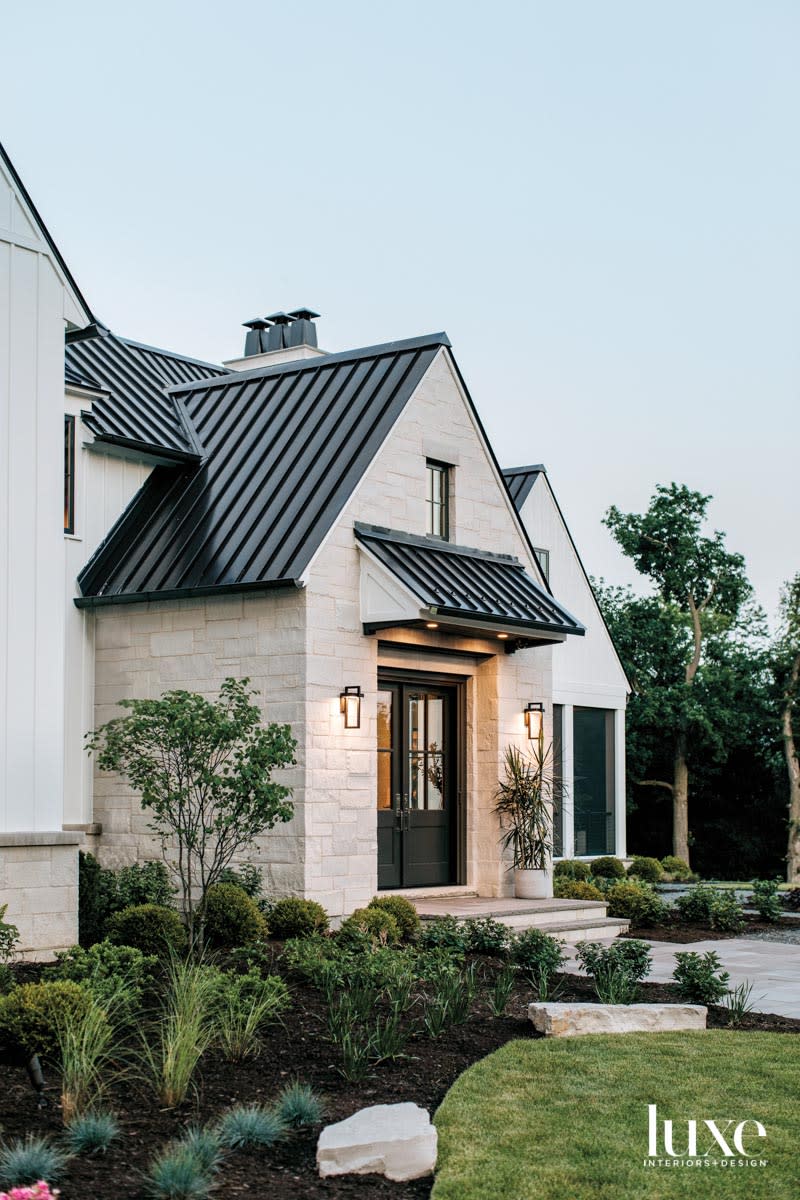 The front exterior of a limestone residence with a black aluminum roof.