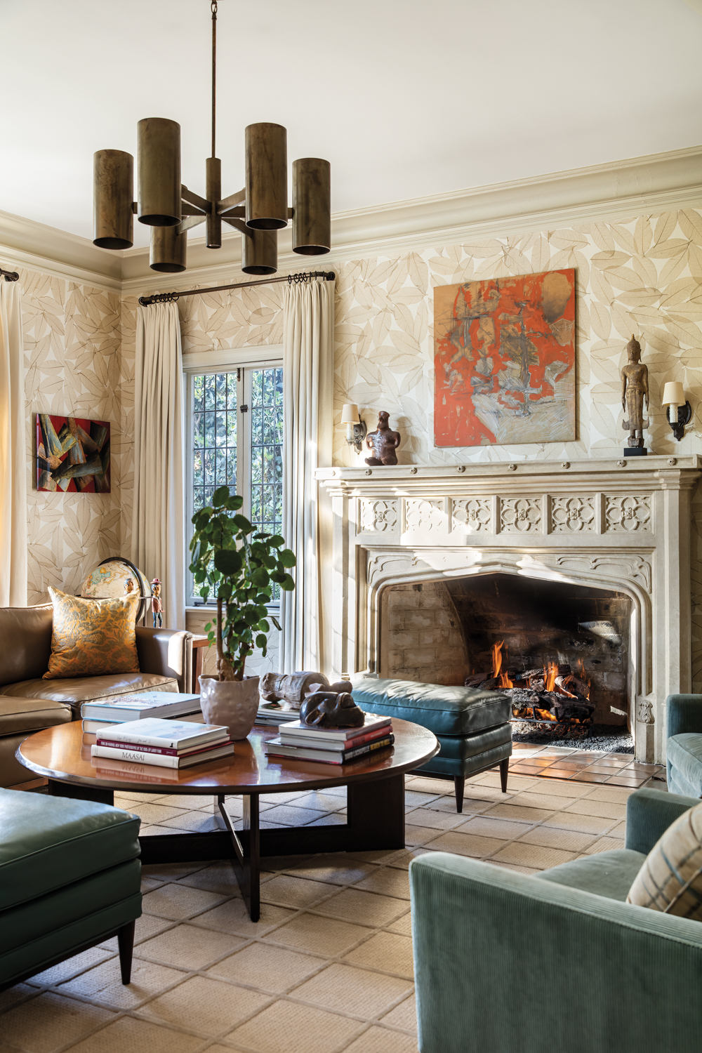 Family room with leaf-pattern, white-and-gold wallpaper, carved fireplace and vintage chandelier.