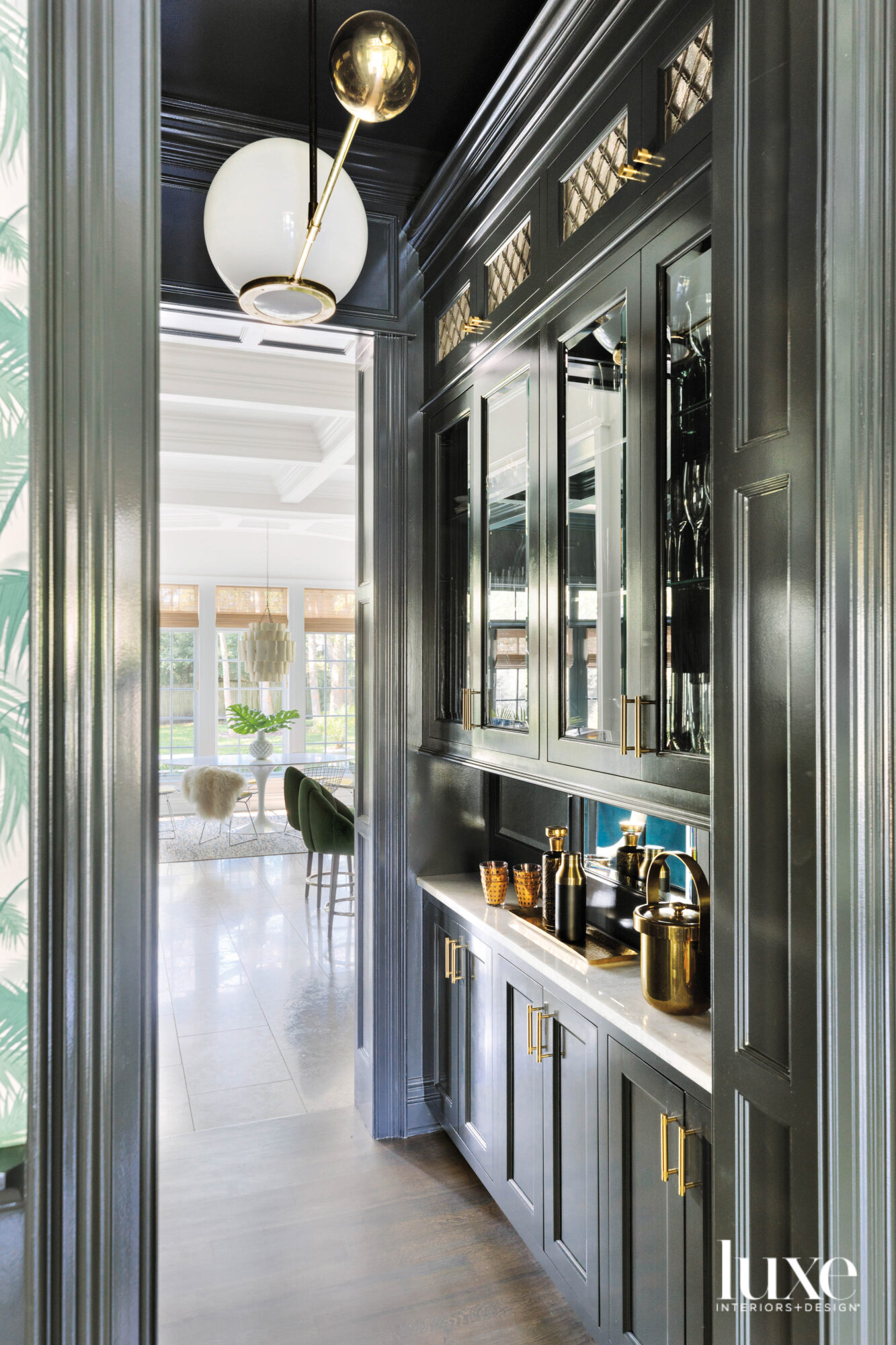 A cocktail pantry painted in black. The cabinets have brass hardware.