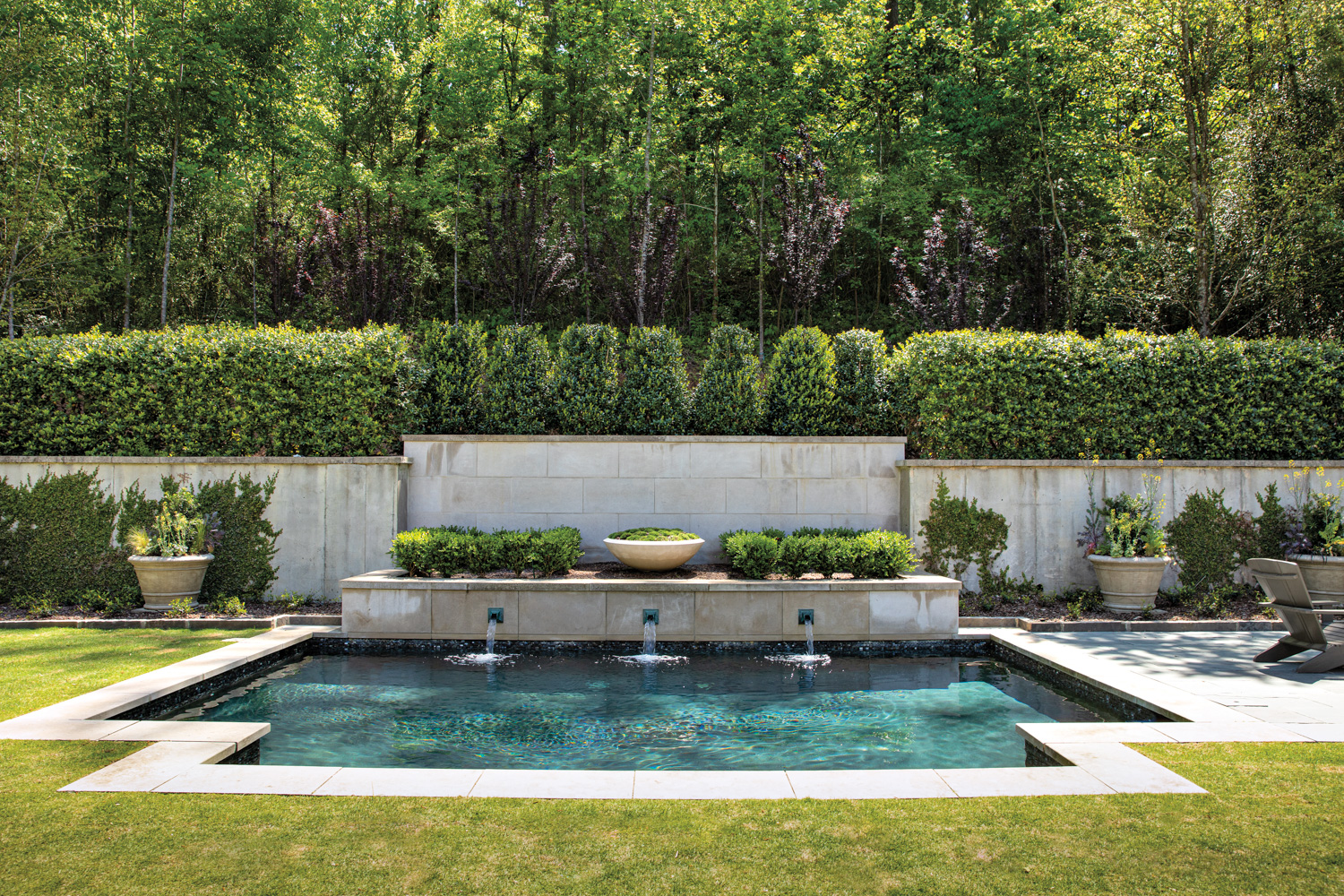 Swimming pool with fountain, trimmed grass and boxwood border showcases formal garden design style