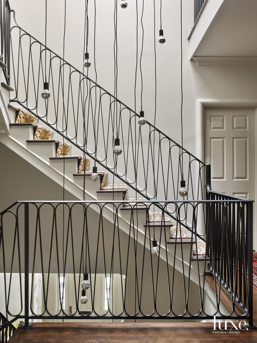 staircase with decorative iron railing and numerous hanging bulbs