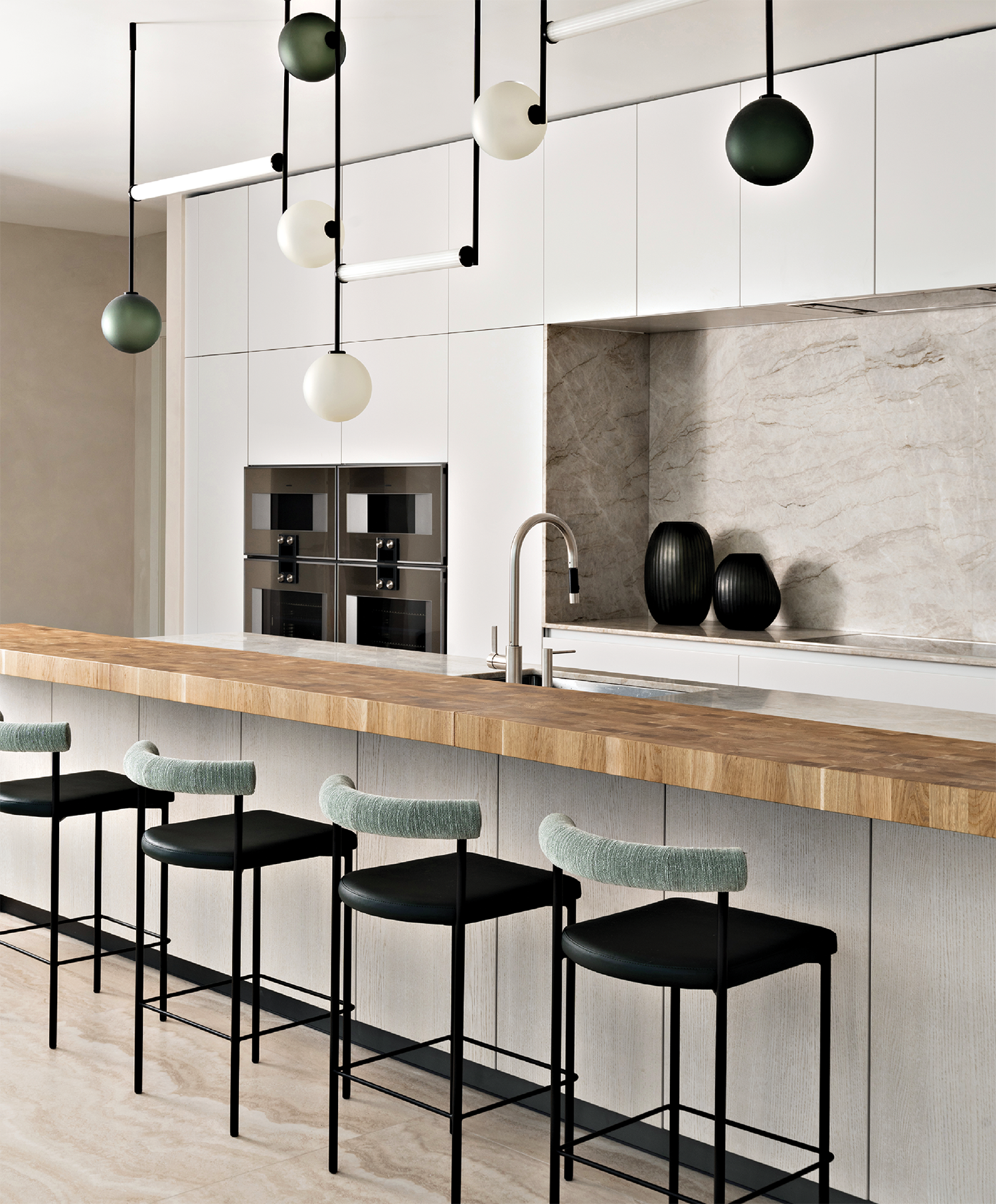 modern white kitchen with a butcher block island beneath planetary-like pendants
