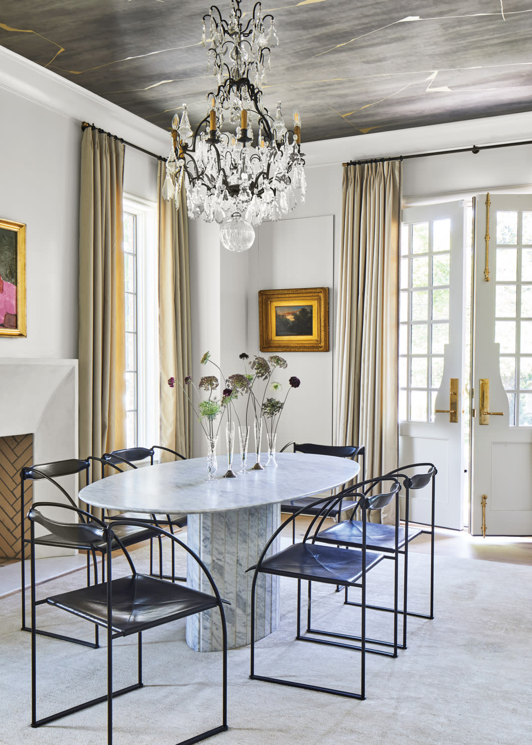 Glamorous dining room featuring an elliptical marble table, metal-framed dining chairs and a Rococo crystal chandelier