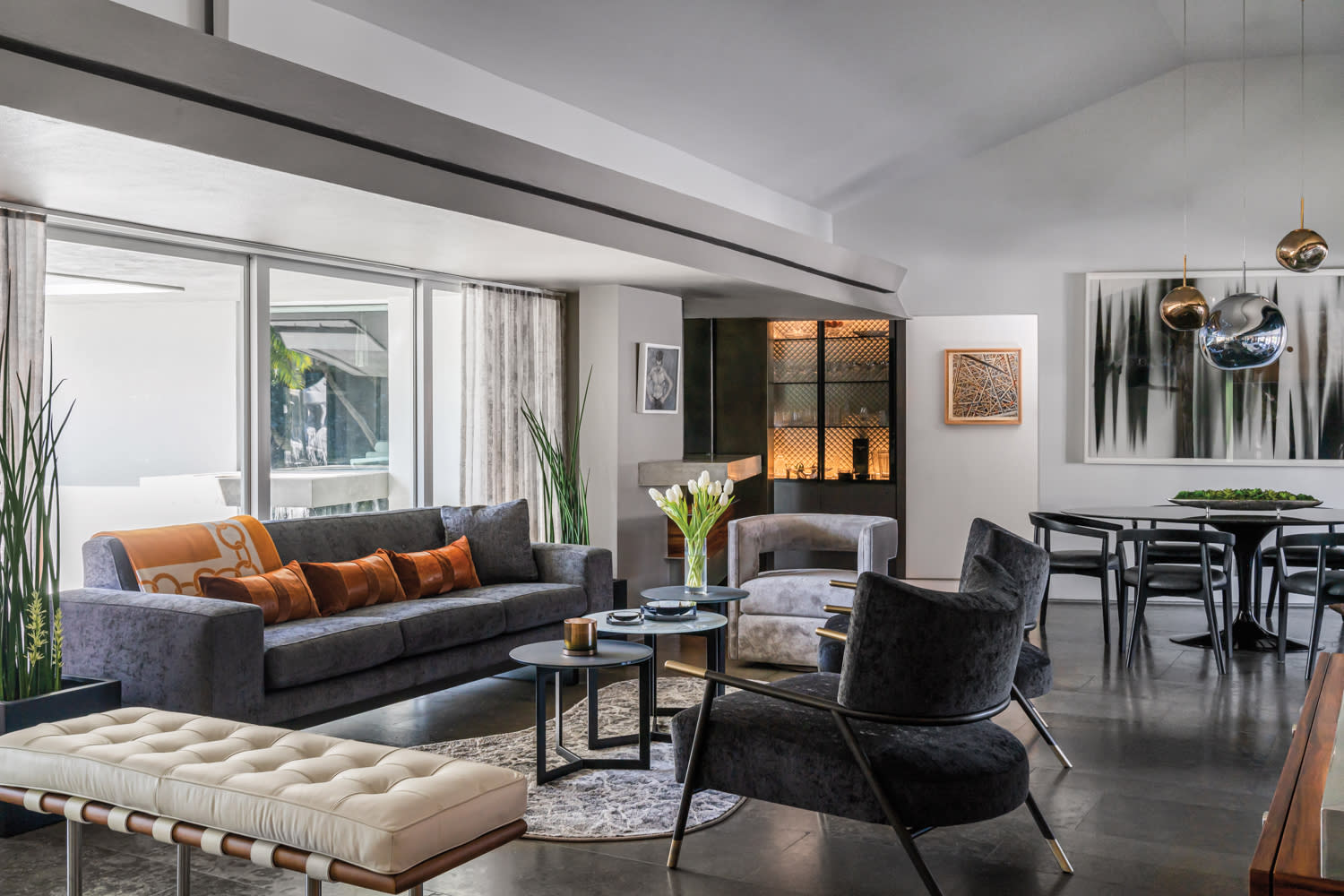 living room with tufted bench, dark sofa and round coffee tables atop a curvy rug and dark flooring