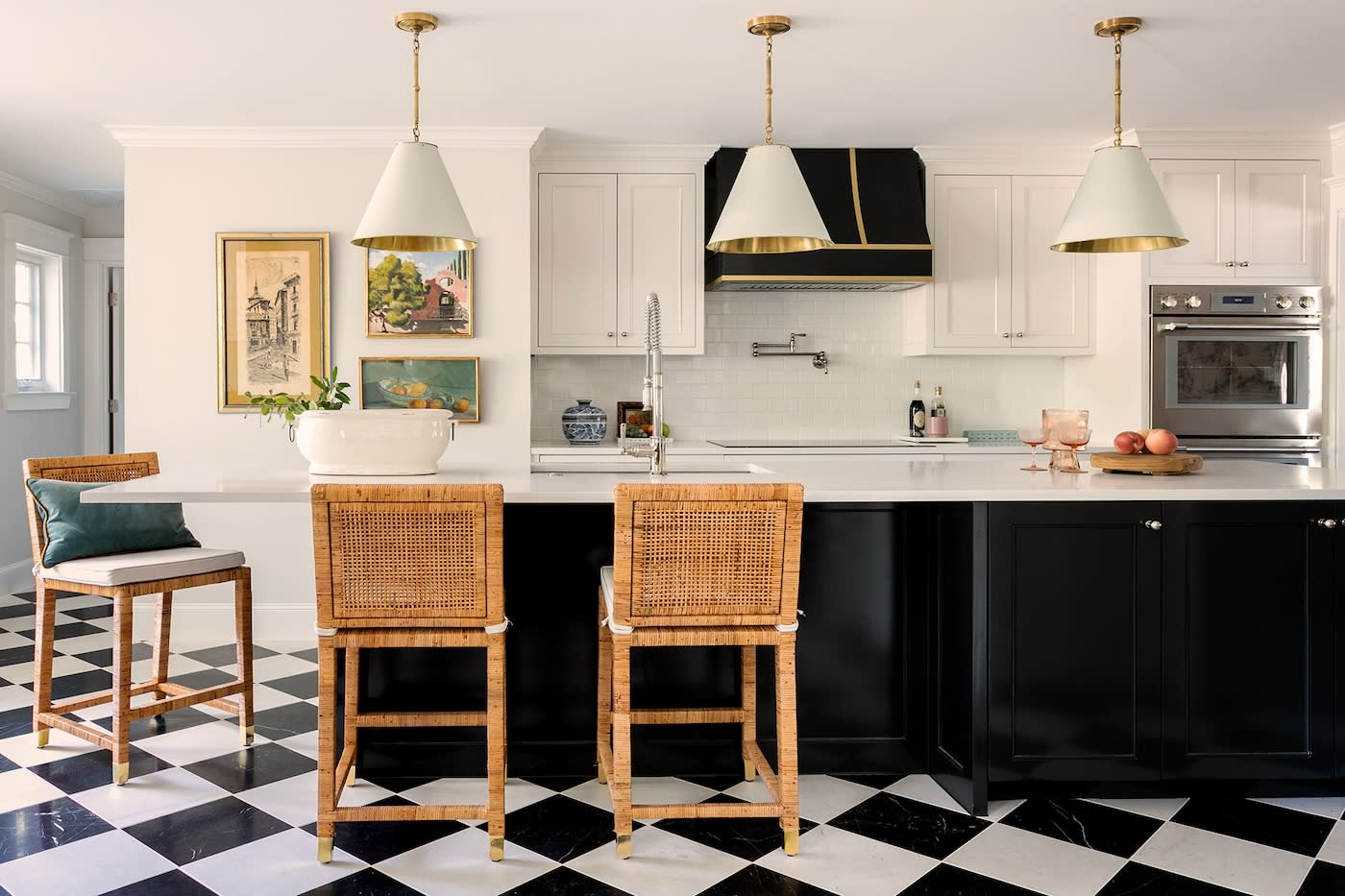 A stylish kitchen with a black and white checkered floor, three wicker bar stools, black island, and white cabinets. Pendant lights add elegance.