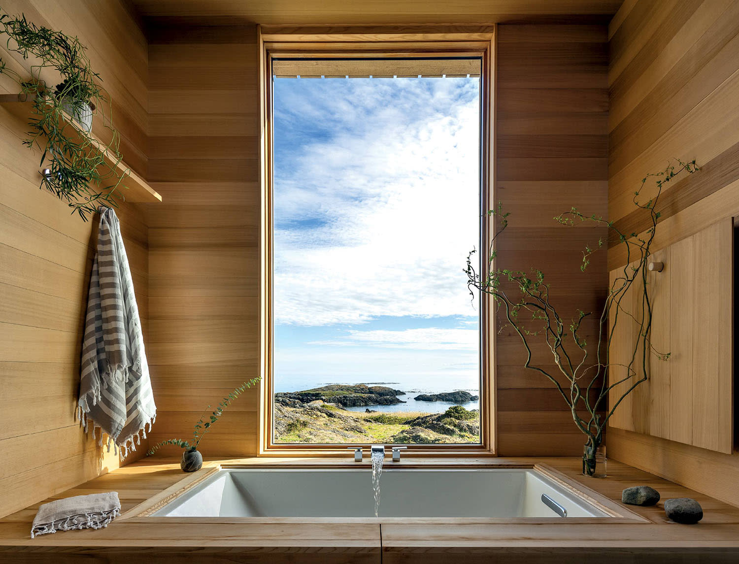 A bathtub with a custom cedar surround, waterfall faucet and a window with water views.