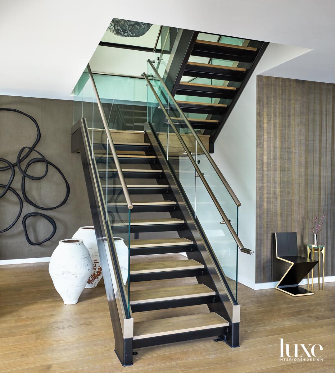 A glass staircase. Behind it are two large white pots and a circular black sculpture on the wall.