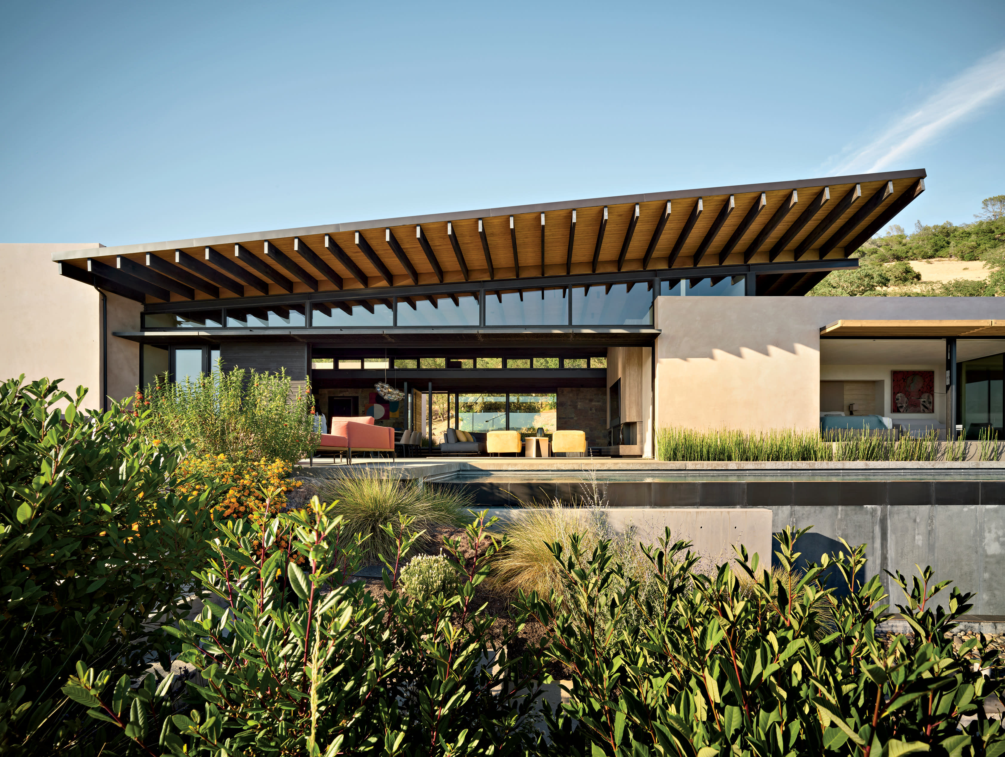 The exterior of the home with a slanted roof shading over a terrace with seating and landscaping.