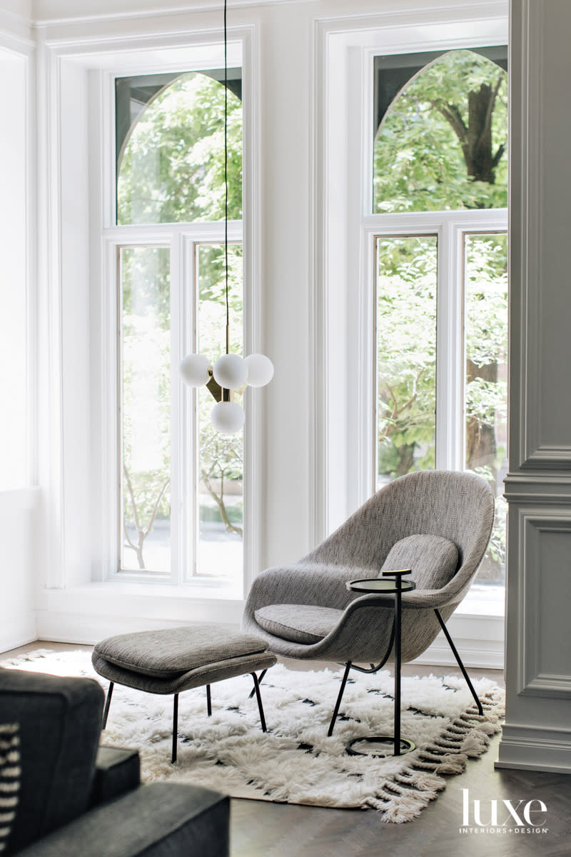 A corner seating area with a midcentury modern style chair and ottoman by floor-to-ceiling windows.