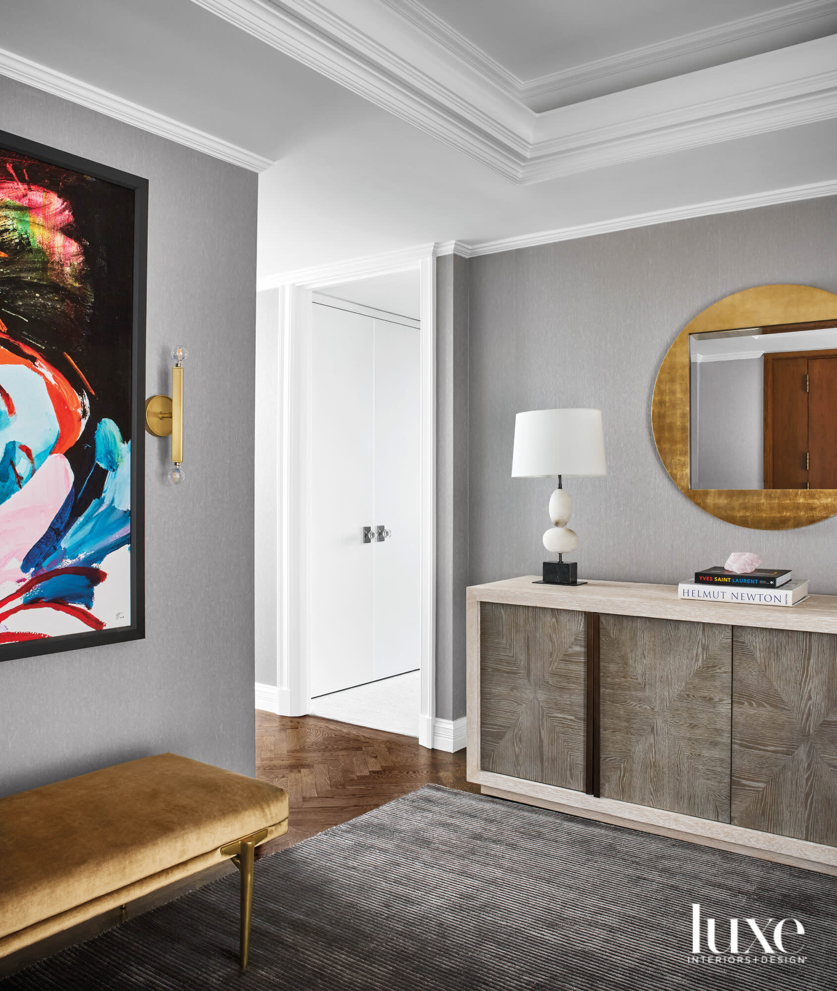 A gray entry with a gold round mirror and a bright neon painting.