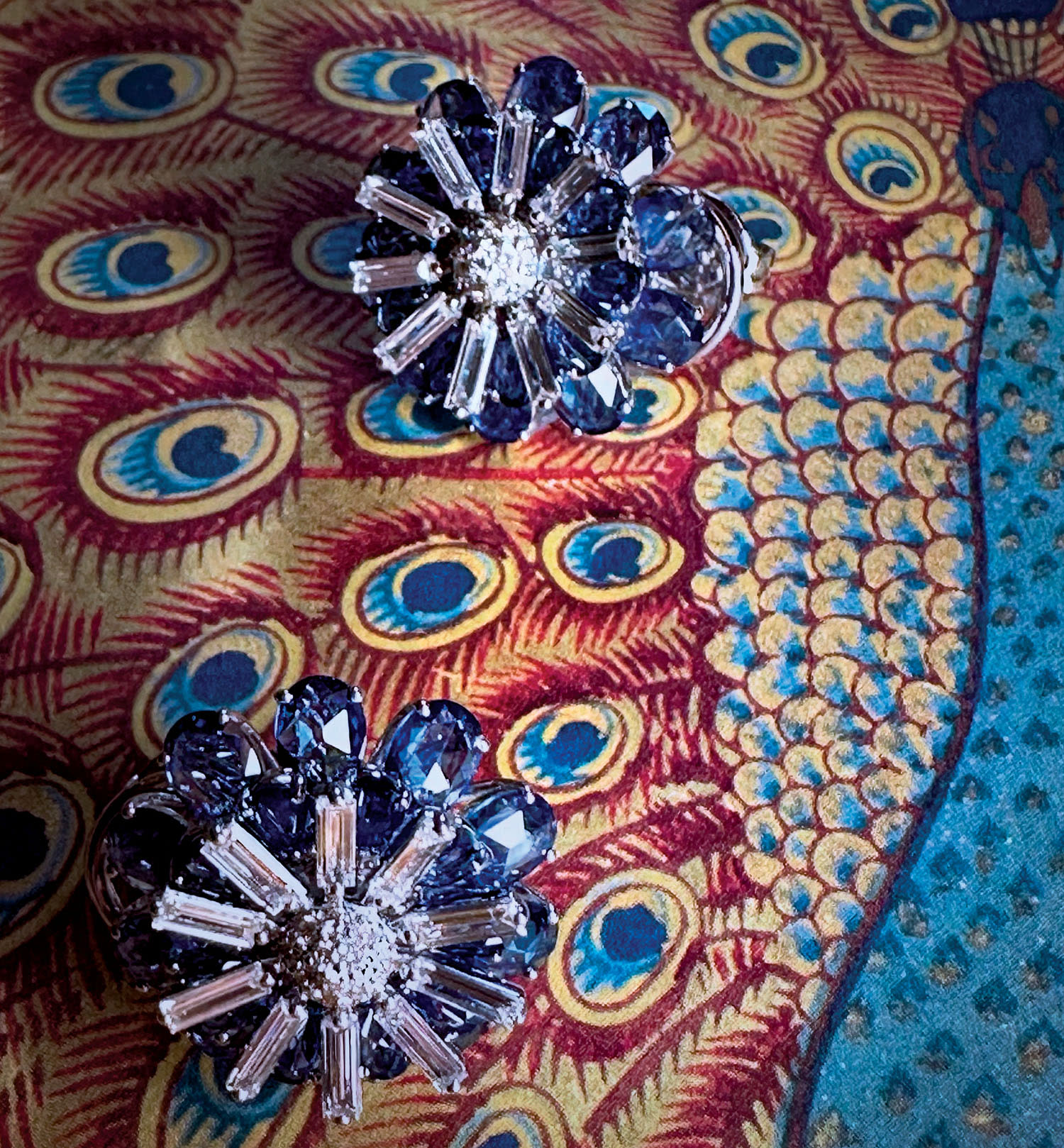 Sapphire earrings in a starburst pattern sit on red-and-blue peacock patterned fabric.