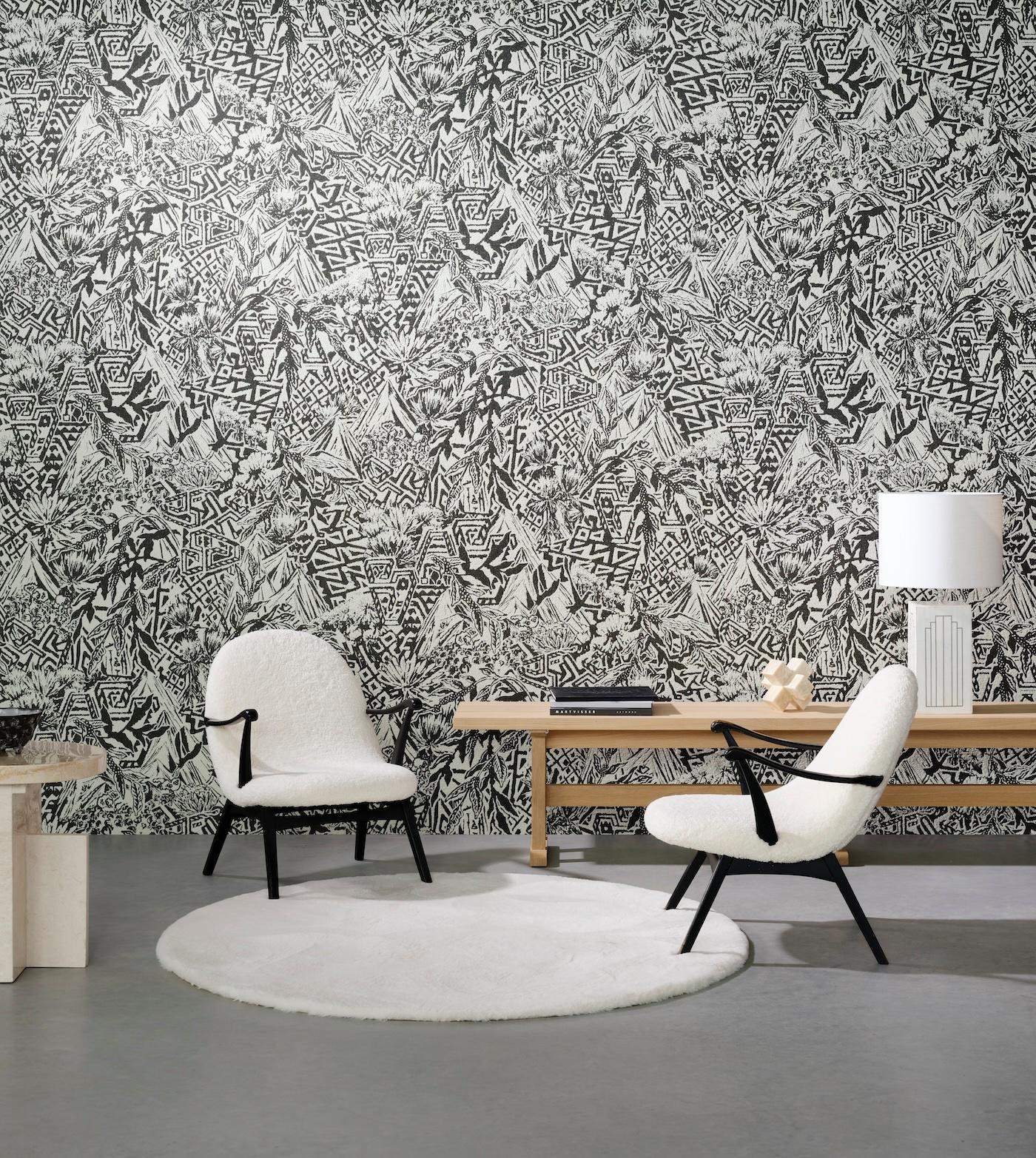 Modern living room with two white cushioned chairs on a round white rug. Abstract black and white patterned wall, wooden table, and lamp. Cozy ambiance.